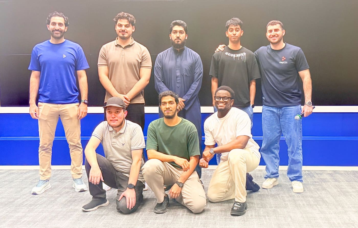 Eight people posed together in a lecture room at the end of a build event, one holding a microphone.