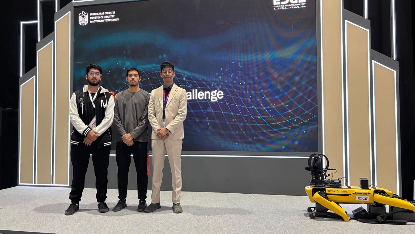 Three team members standing on the Industry Challenge stage beside a yellow Boston Dynamics Spot robot, under a UAE Ministry of Industry and Advanced Technology screen.