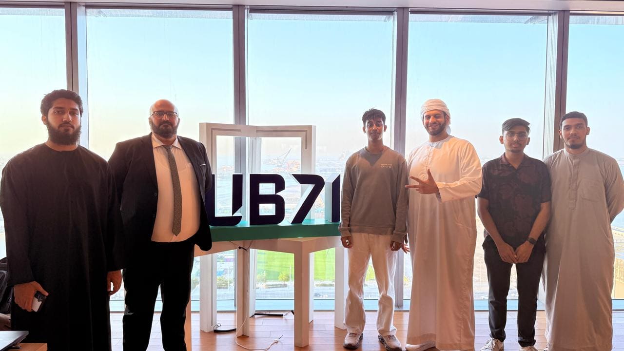 Six people standing either side of a large Hub71 logo sculpture in a room overlooking Abu Dhabi.