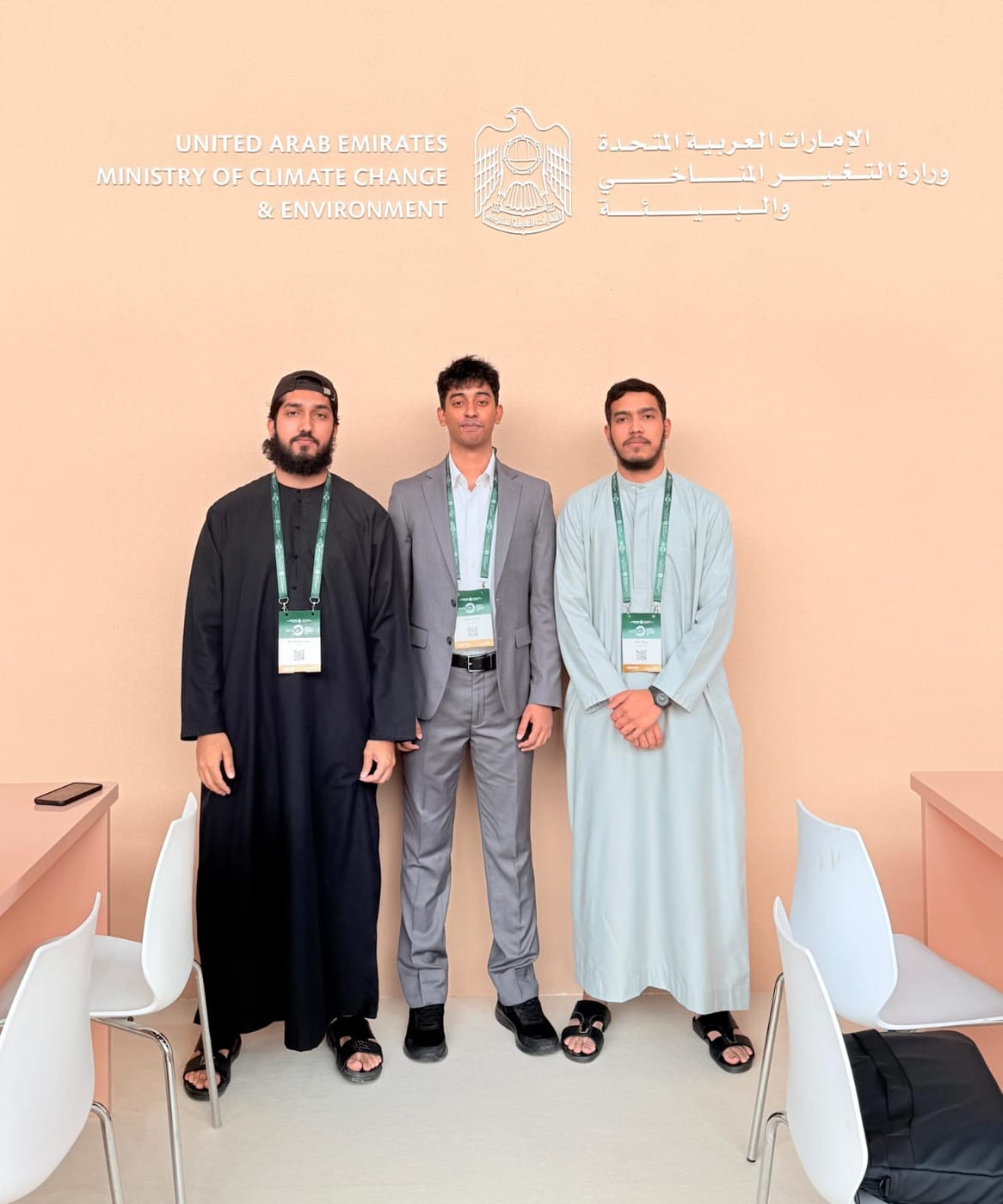 Three people standing under a wall sign reading 'United Arab Emirates Ministry of Climate Change & Environment', wearing green conference lanyards.
