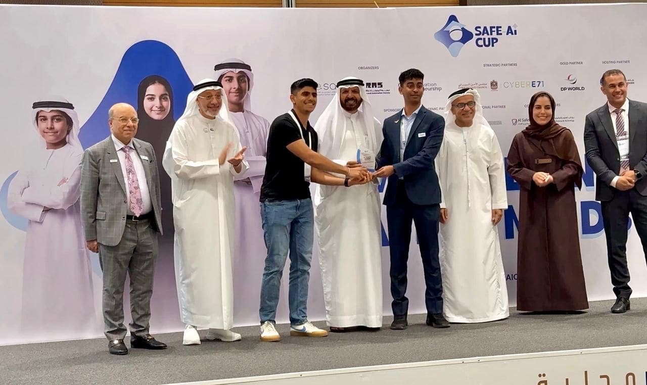 A trophy being handed over on the Safe AI Cup stage, with a backdrop listing the organisers and partners.