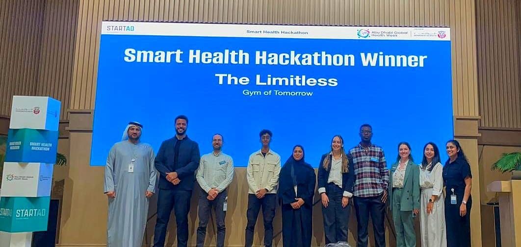 A stage screen reading 'Smart Health Hackathon Winner - The Limitless, Gym of Tomorrow', with the team and organisers lined up in front of it.